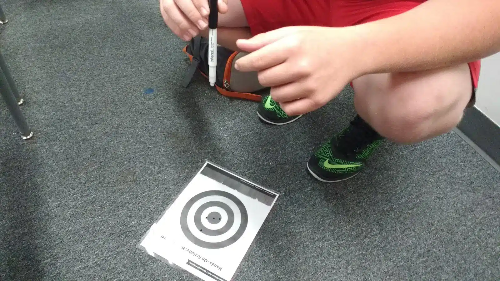 student holding dry erase marker over hit the target lab paper. 