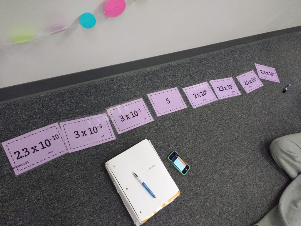 scientific notation ordering cards laying in row on floor of classroom.