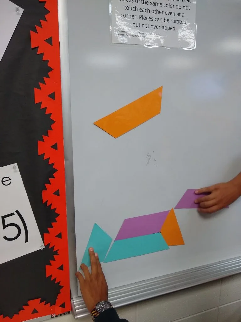 Students attempting to solve equilateral triangle puzzle on dry erase board 
