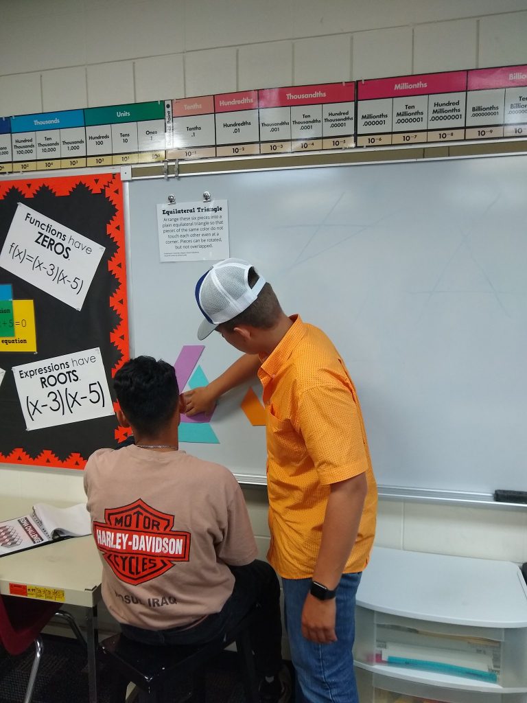 Students attempting to solve equilateral triangle puzzle on dry erase board 