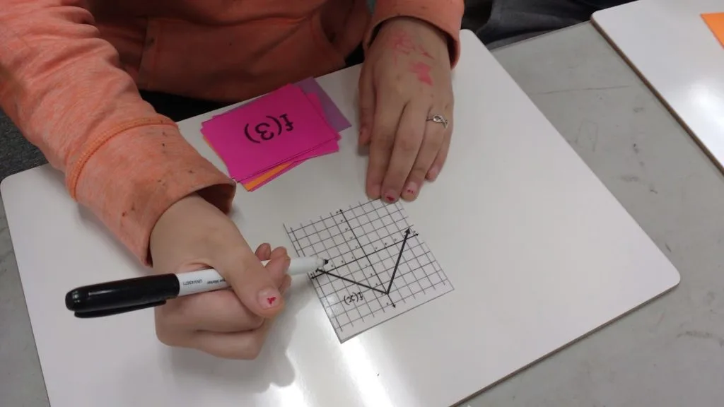 student pointing dry erase marker at graph card during game of evaluating functions war activity 