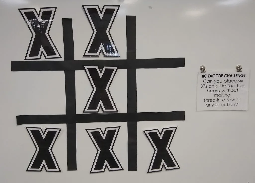 jumbo version of tic tac toe puzzle hanging on dry erase board with magnets 