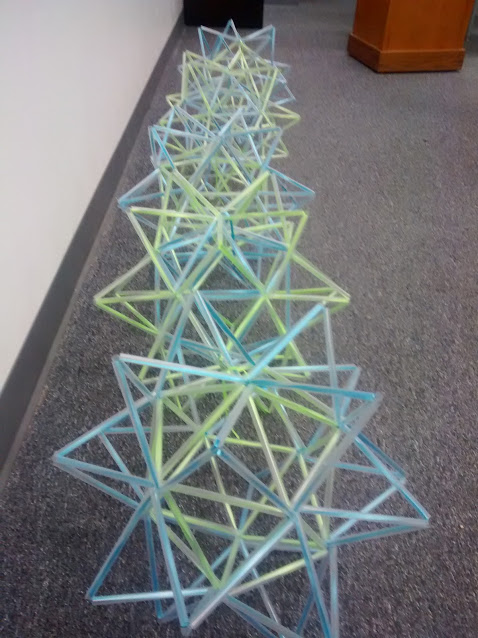 stellated icosahedron straw art sitting in row on floor of classroom. 
