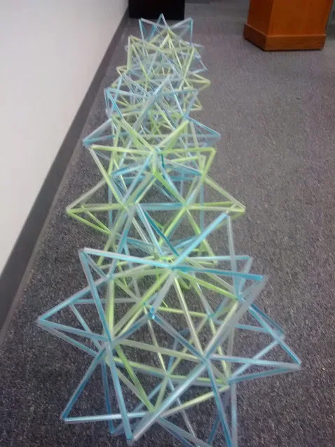 stellated icosahedron straw art sitting in row on floor of classroom. 