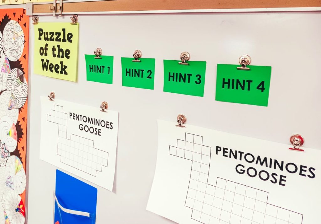 pentominoes goose puzzle hanging up on dry erase board in high school math classroom with hint cards 