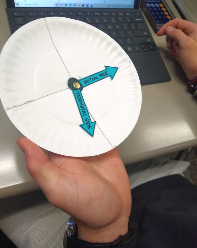 student holding paper plate angle spinner while working on desmos assignment on chromebook