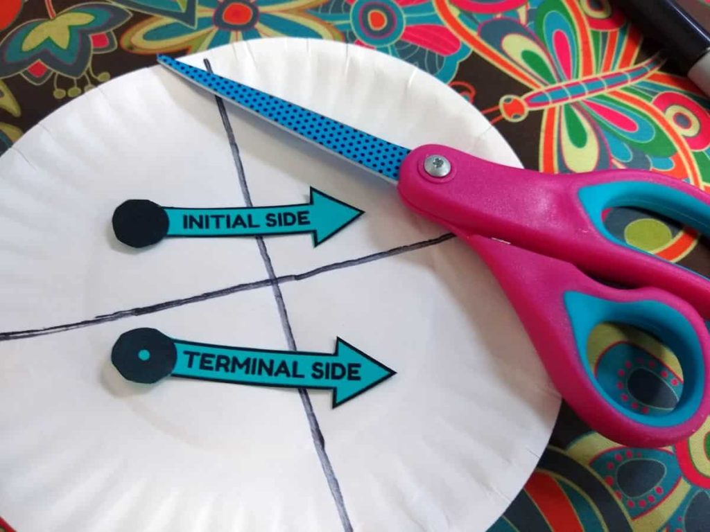 partially built paper plate angle spinner with terminal side and initial side cut out of cardstock and scissors laying on top of the plate 