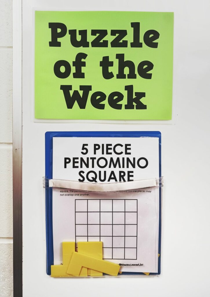 5 piece pentomino square puzzle hanging in magnetic pocket under sign reading "puzzle of the week" 