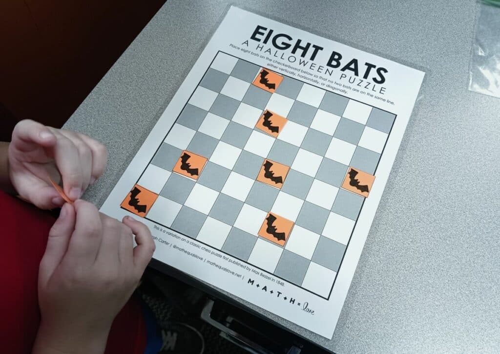 hands of child working to solve 8 bats halloween logic puzzle .