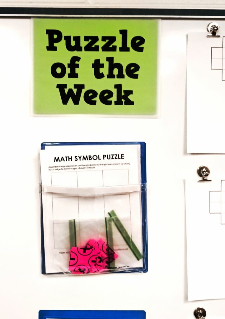 math symbol square puzzle hanging under sign reading "puzzle of the week" 