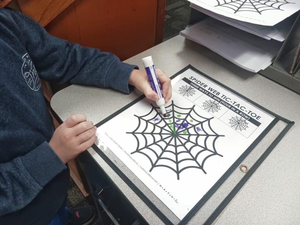 child playing spider web tic tac toe game in dry erase pocket for halloween. 