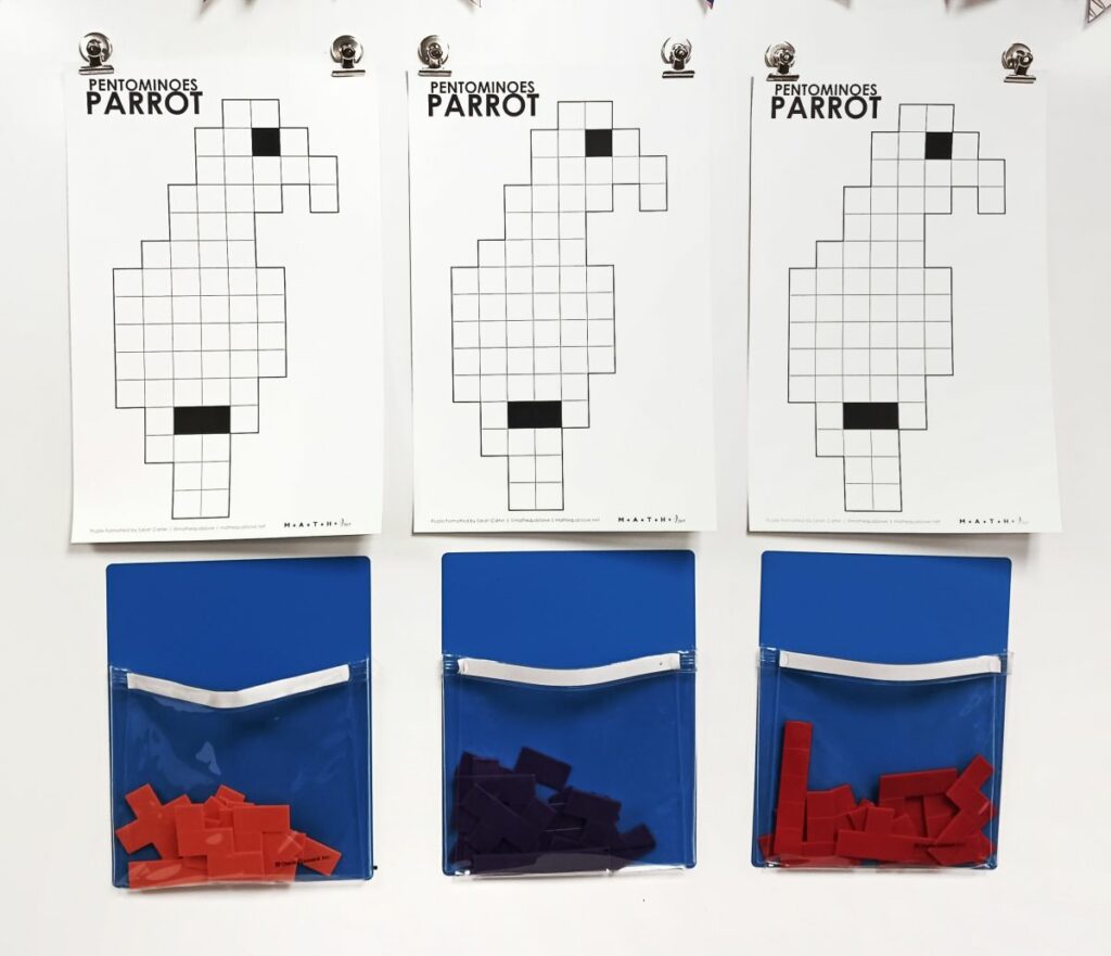 pentomino parrot puzzles hanging on dry erase board with pentominoes in blue pockets under puzzle. 